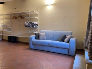 Ein Wohnzimmer mit einer Couch, Regalen mit Kleidung und einem Fliesenboden.