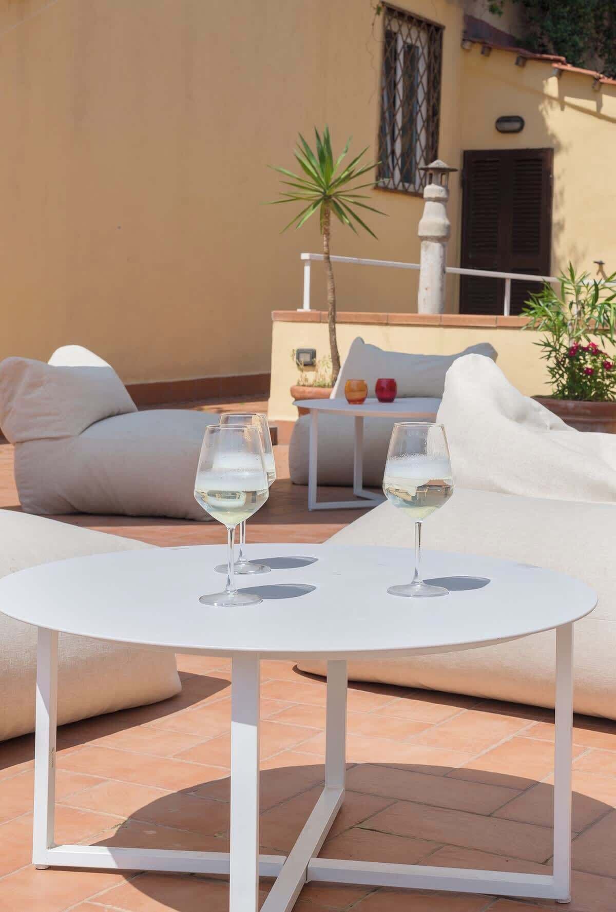Zona salotto all'aperto con due tavoli bianchi, ognuno con un bicchiere di vino bianco.
