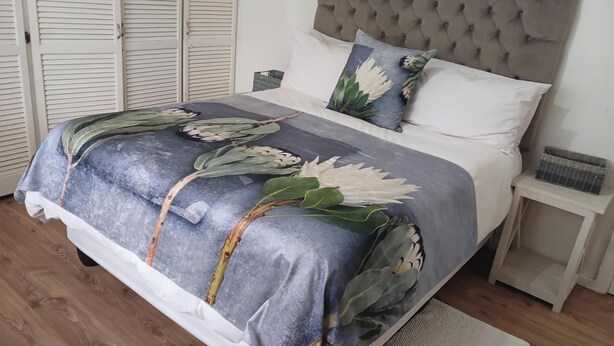 Una cama con cubrecama floral, cabecero acolchado y mesita de noche con una cesta.