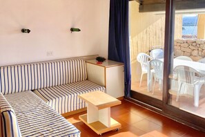 Ein Zimmer mit einem gestreiften Sofa, einem kleinen Holztisch und einer Glastür, die zu einem Außenbereich mit Stühlen und einem Tisch führt.
