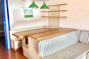 Ein Schlafsofa mit Stoffbezug in Streifenoptik, ein Holztisch und zwei grüne Pendelleuchten.