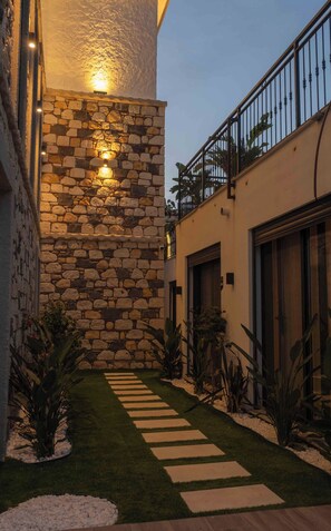 A stone wall with a stone pathway leading to a building entrance, surrounded by greenery and a metal railing. - Canata Hotel Çeşme (Cesme)