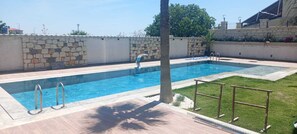 A rectangular swimming pool with a stone wall and a grassy area with a palm tree. - Canata Çeşme (İzmir)