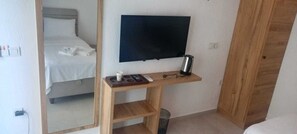 A hotel room with a bed, a TV mounted on the wall, a wooden console table with a remote control, and a trash bin. - Canata Çeşme (İzmir)