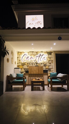 L’entrée de l’hôtel est ornée d’un mur en pierre et d’une enseigne au néon sur laquelle on peut lire « Can Ata ». On y trouve deux canapés en bois avec des coussins, ainsi qu’une petite table en bois placée devant.