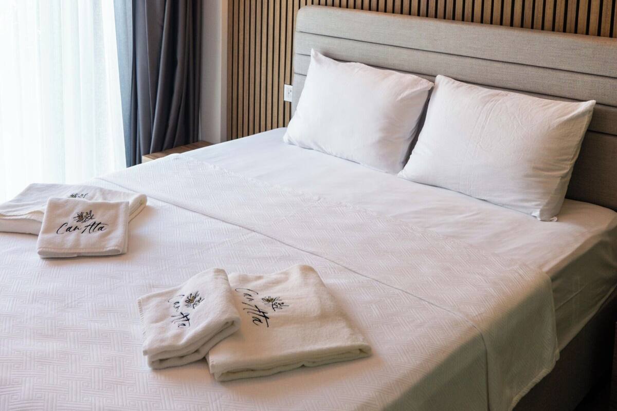 A hotel room with a large bed, a hanging light fixture, a wall-mounted lamp, and a window with curtains.