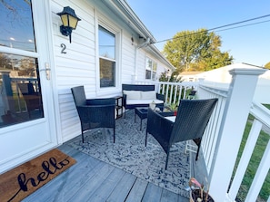A porch with wicker furniture, a doormat, and a white fence.