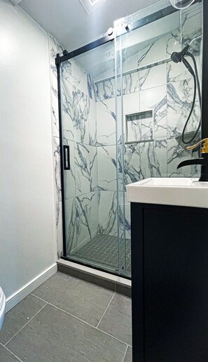 A bathroom with a glass shower door, a sink with a gold faucet, and marble-patterned walls. - The perfect APT near everything! (Rio grande)