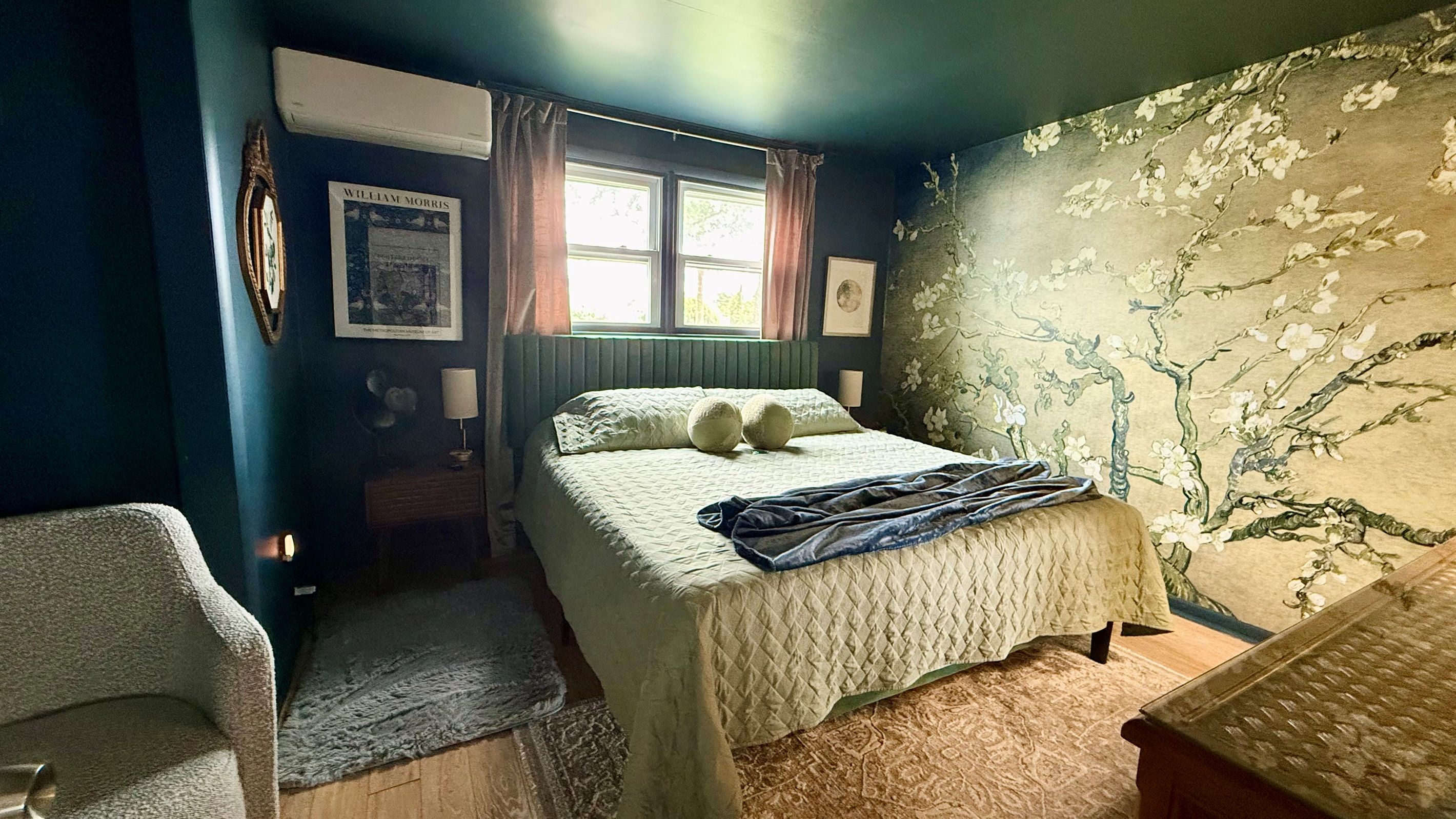 A bedroom with a bed, a chair, a window, and a wall with a floral pattern.