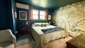 A bedroom with a bed, a chair, a window, and a wall with a floral pattern.