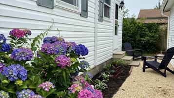 A white house with green shutters, a gravel patio, and a garden with hydrangea flowers.