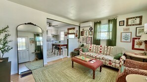 A living room with a sofa, a dining table, and a kitchen in the background. - Charming 2BR, steps to Hawk Haven, near Beaches (rio grande)