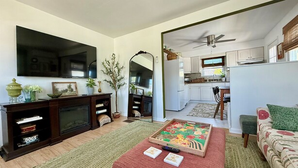A living room with a TV, fireplace, and a kitchen visible through an open door. - Botanical 2BR, steps to Hawk Haven, near Beaches (rio grande)