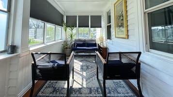 A sunroom with a sofa, two chairs, a patterned rug, and a potted plant.