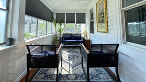 Ein Wintergarten mit einer Couch, zwei Sesseln, einem gemusterten Teppich und einer Topfpflanze.