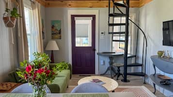 A cozy room with a green couch, a small table, a purple door, and a spiral staircase.