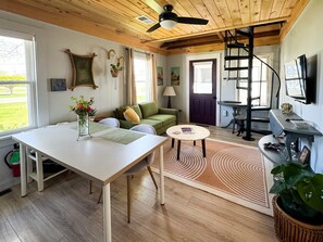 Ein gemütliches Wohnzimmer mit Holzboden, einem Esstisch, einer Couch, einem Fernseher und einer Treppe, die zu einer anderen Ebene führt.