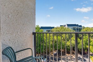 Ein Balkon mit Metallgeländer, einem Stuhl und Blick auf Gebäude und Bäume.