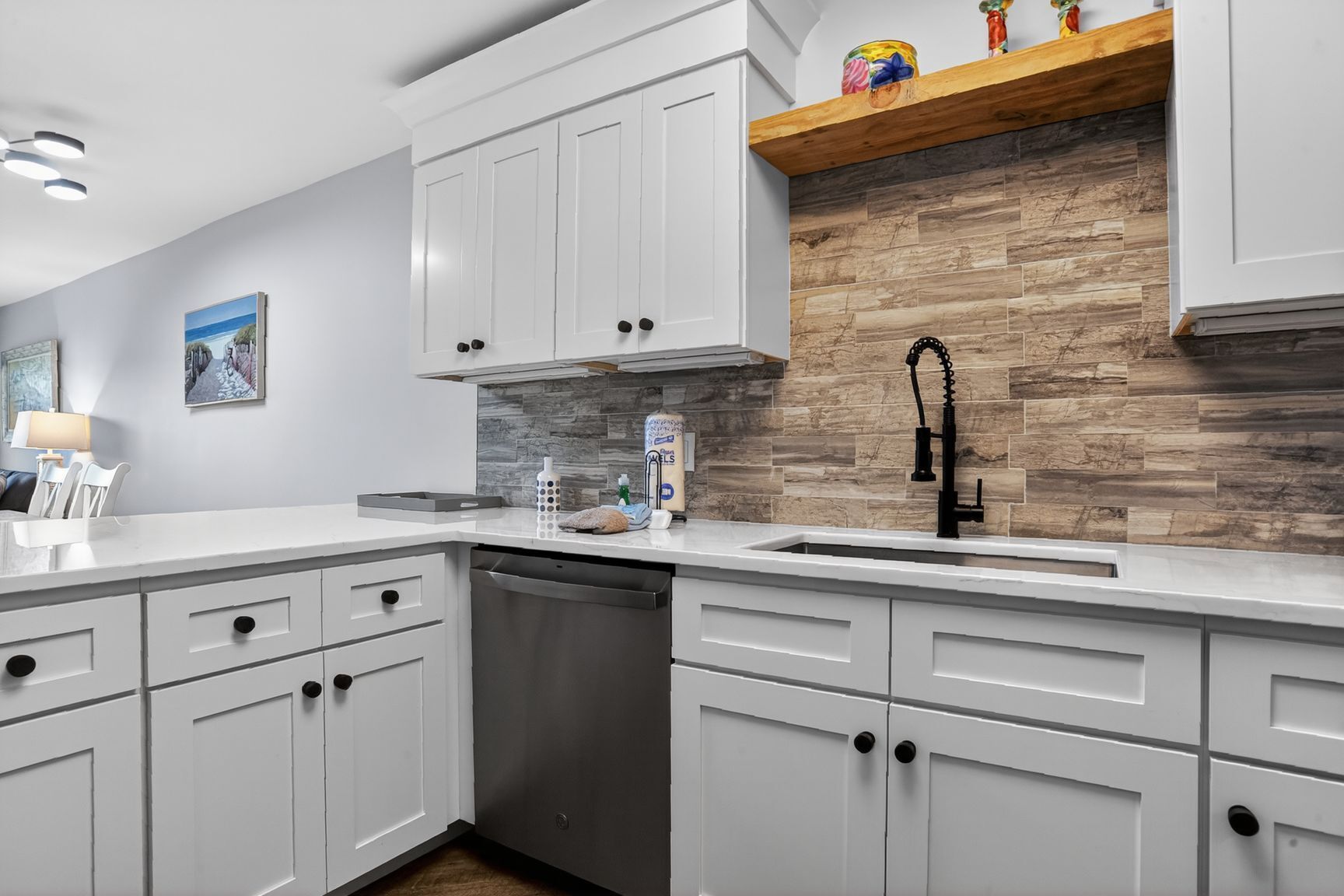 A modern kitchen with white cabinetry, a wooden backsplash, and a stainless steel dishwasher.