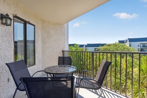 Een balkon met een tafel, stoelen, een raam en uitzicht op omliggende gebouwen en groen.