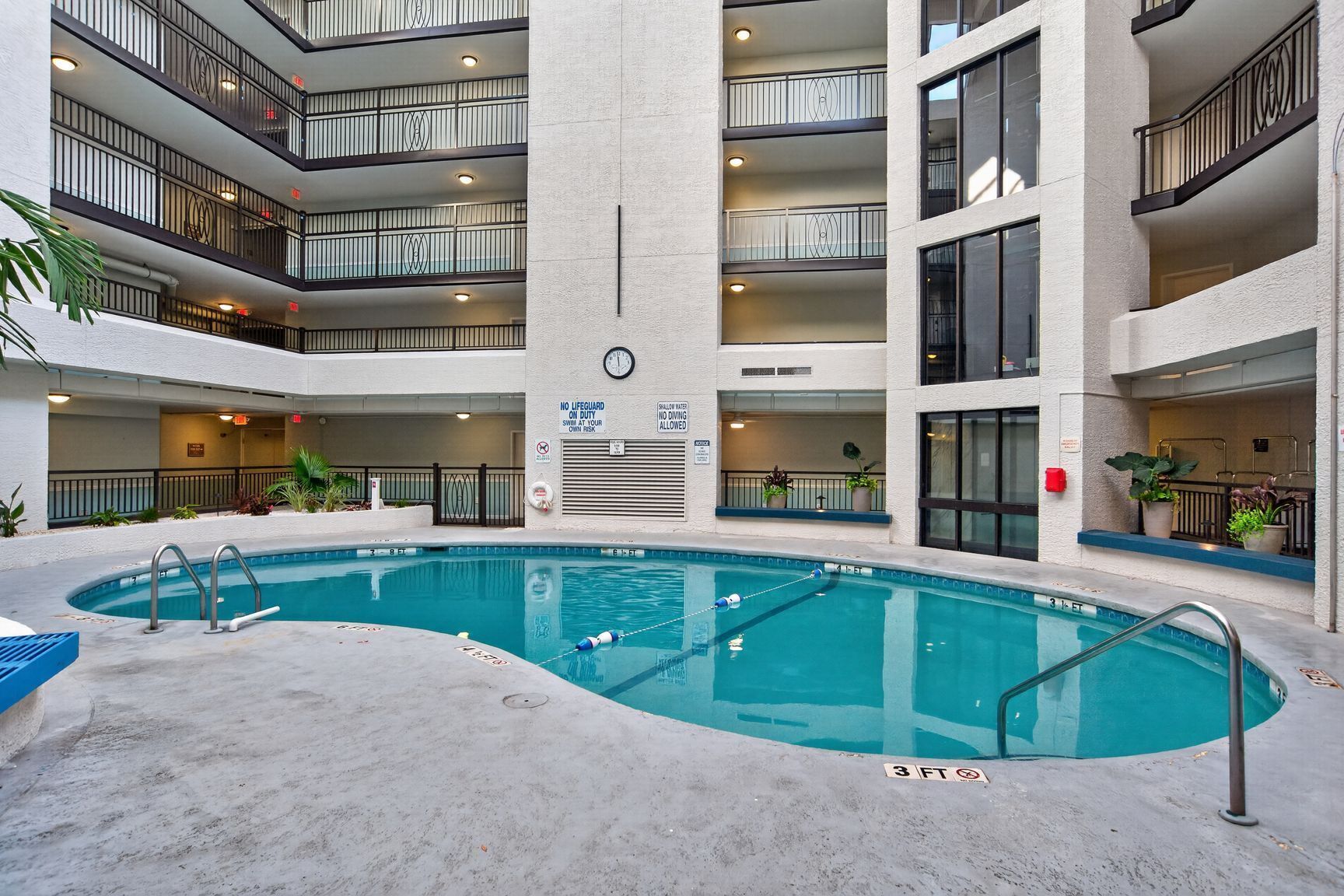 An indoor swimming pool with multiple balconies, a clock, and a lifeguard sign.