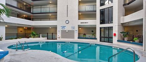 An indoor swimming pool with multiple balconies, a clock, and a lifeguard sign.