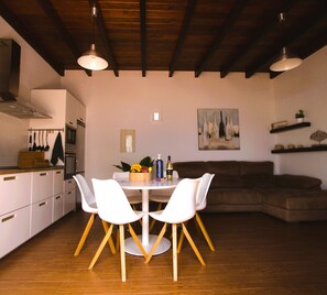 A modern kitchen with white cabinets, a dining table with two chairs, a brown sofa, and a painting on the wall. - Cozy and bright house in a central area of the island. (Tías)