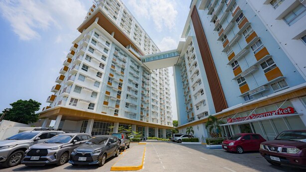 A high-rise building with multiple floors, a parking area with several cars, and a visible storefront with a sign. - Cozy Stay at Casa Mira Towers Guadalupe (Cebu City)