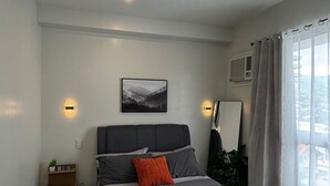 A modern bedroom with a large bed, bedside tables, a wall-mounted mirror, and a ceiling light fixture. - Cozy Stay at Casa Mira Towers Guadalupe (Cebu City)