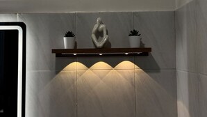 A bathroom with a white tiled wall, a wooden shelf with two potted plants, and a white statue. - Cozy Stay at Casa Mira Towers Guadalupe (Cebu City)