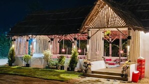 Una estructura de madera con techo de paja, una zona de estar cubierta y plantas en macetas.
