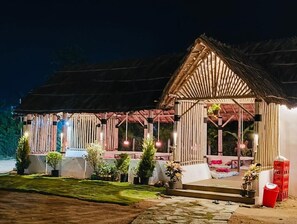 A wooden structure with a thatched roof, a covered seating area, and potted plants.