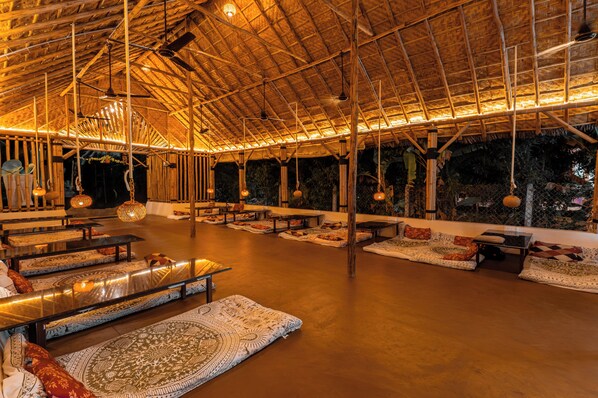 An indoor space with a high ceiling, wooden beams, hanging lights, and patterned rugs.