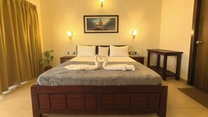 Habitación de hotel con una cama grande, dos mesitas de noche, una lámpara de noche, una planta en maceta y una puerta.