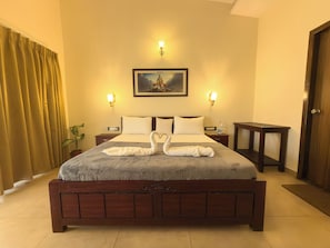 Habitación de hotel con una cama grande, dos mesitas de noche, una lámpara de noche, una planta en maceta y una puerta.