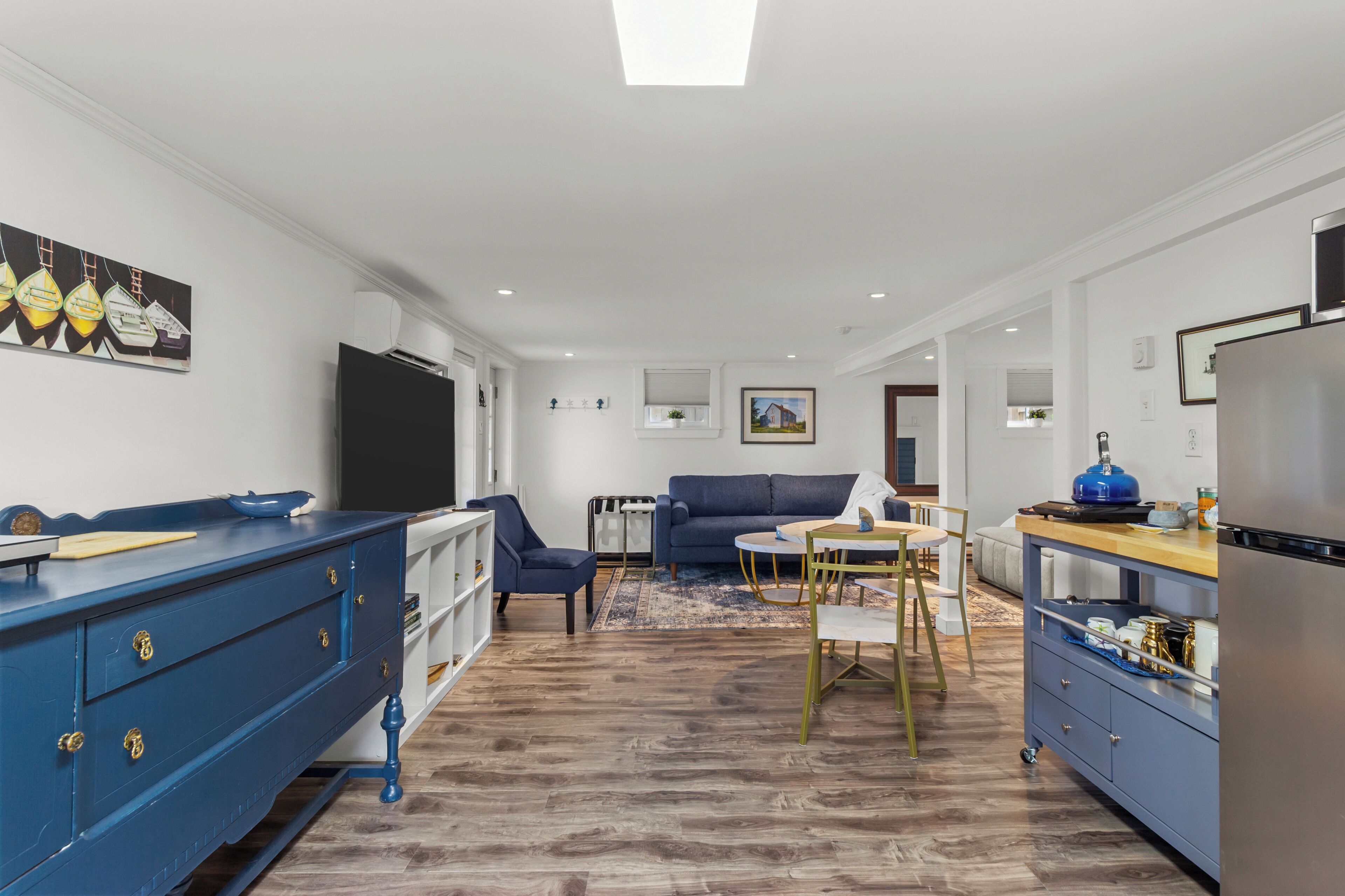 Un salon moderne avec un canapé bleu, une table à manger et un coin cuisine équipé d’un réfrigérateur.