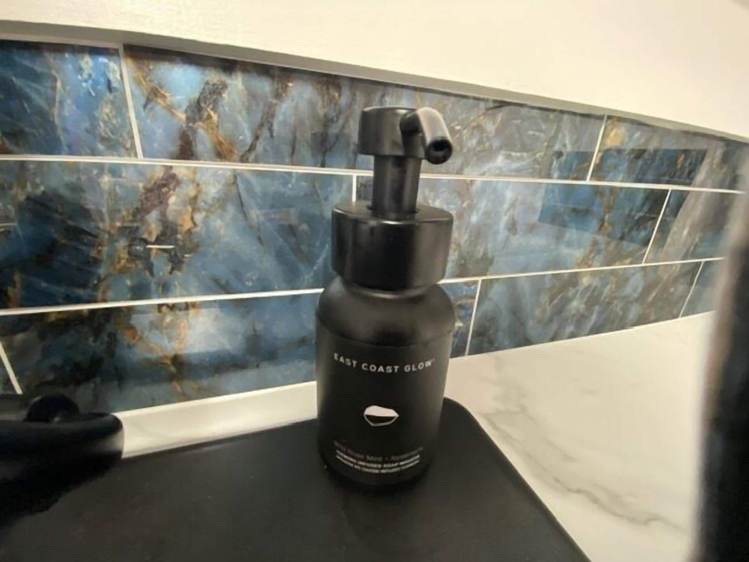 Een badkamer met een zwarte fles met de tekst 'EAST COAST GLOW' op een aanrecht.