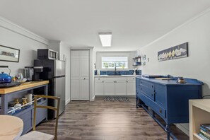 A modern kitchen with white cabinets, a blue dresser, and a window with a view.
