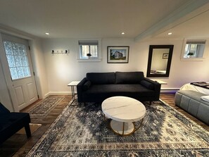 A living room with a dark sofa, a round white table, patterned rugs, and framed pictures on the walls. - The Whistling Kettle | King Studio Near Downtown (St. John's)