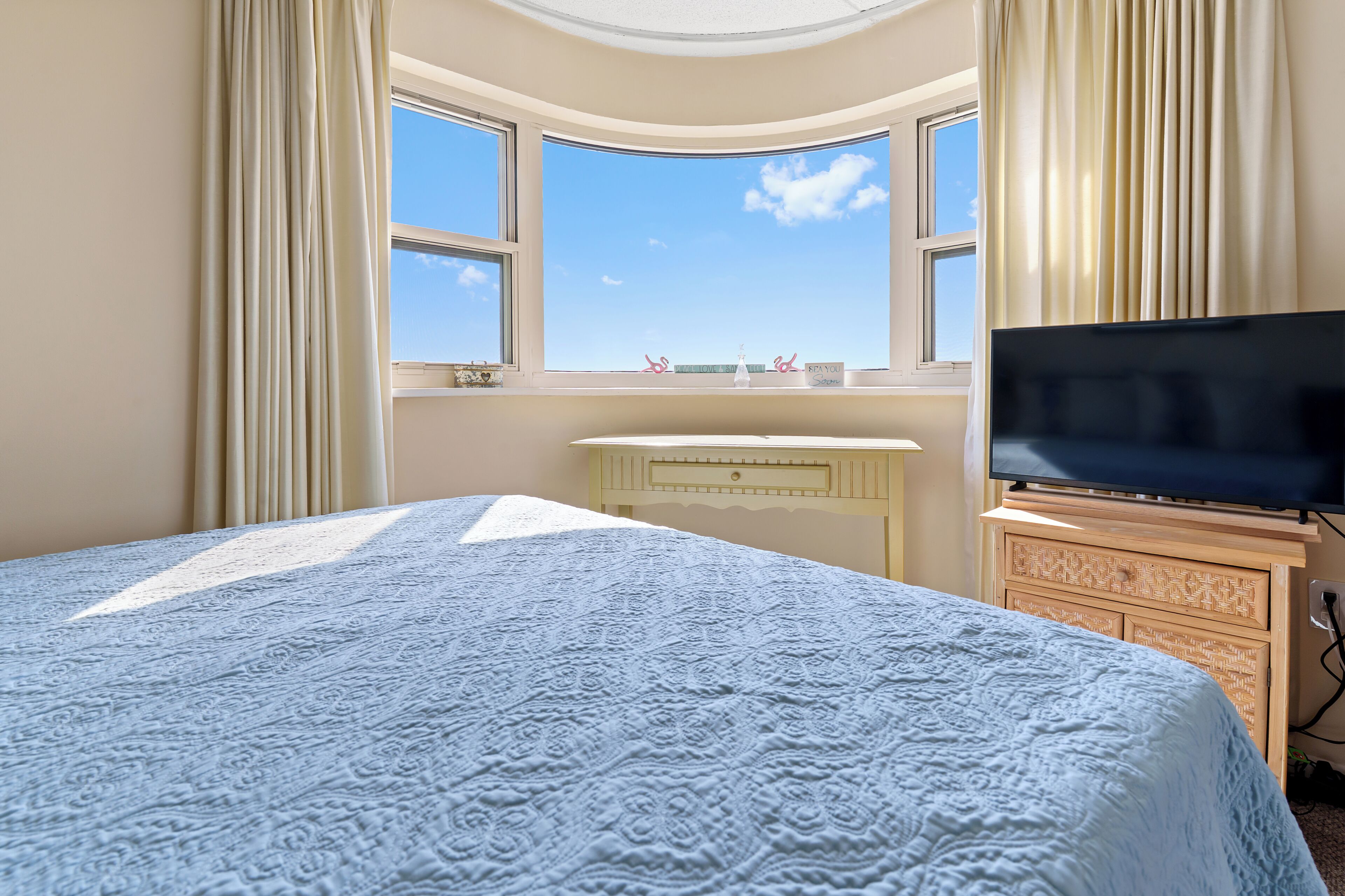 A bedroom with a large bed, a TV, a dresser, and a window with a view.