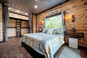 Ein Zimmer mit Holzboden, einem Bett, einem Heizkörper, einem Fenster mit Vorhängen und einem motivierenden Zitat an der Wand.