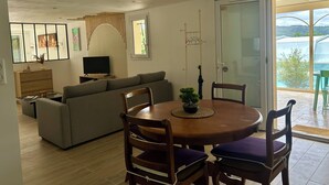 Una sala de estar moderna con un sofá, un televisor, una mesa de comedor con sillas y un ventanal corredizo que da a un balcón.