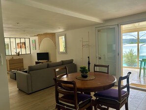 Ein modernes Wohnzimmer mit einer Couch, einem Fernseher, einem Esstisch mit Stühlen und einer Glastür, die auf einen Balkon führt.