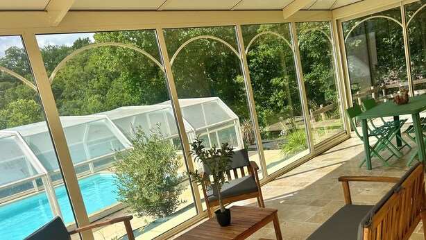 Un patio techado con mobiliario de madera, una piscina e invernadero.