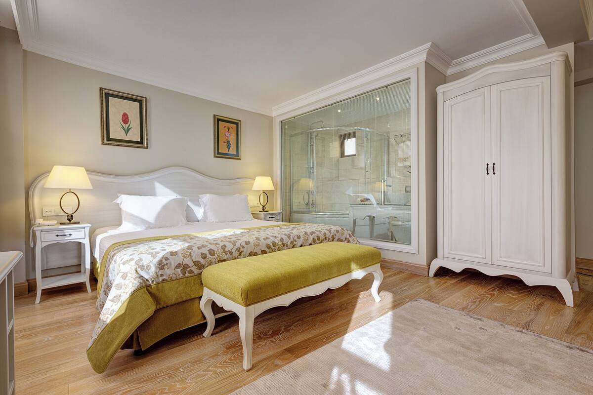 Une chambre à coucher comprenant un lit, des tables de chevet, un banc, une armoire et une cabine de douche en verre.