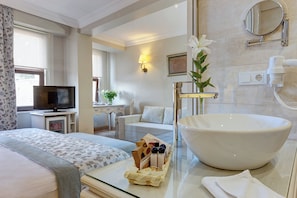 A hotel room with a large white sink, a television, a desk with a lamp, and a bed with floral bedding. - Arena Modern Hotel (Istanbul)
