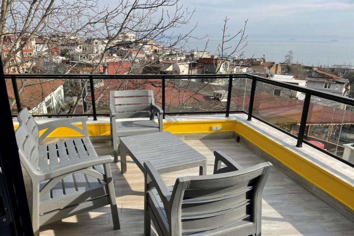 Un balcon avec une table et des chaises, une rambarde jaune et une vue sur le paysage urbain.