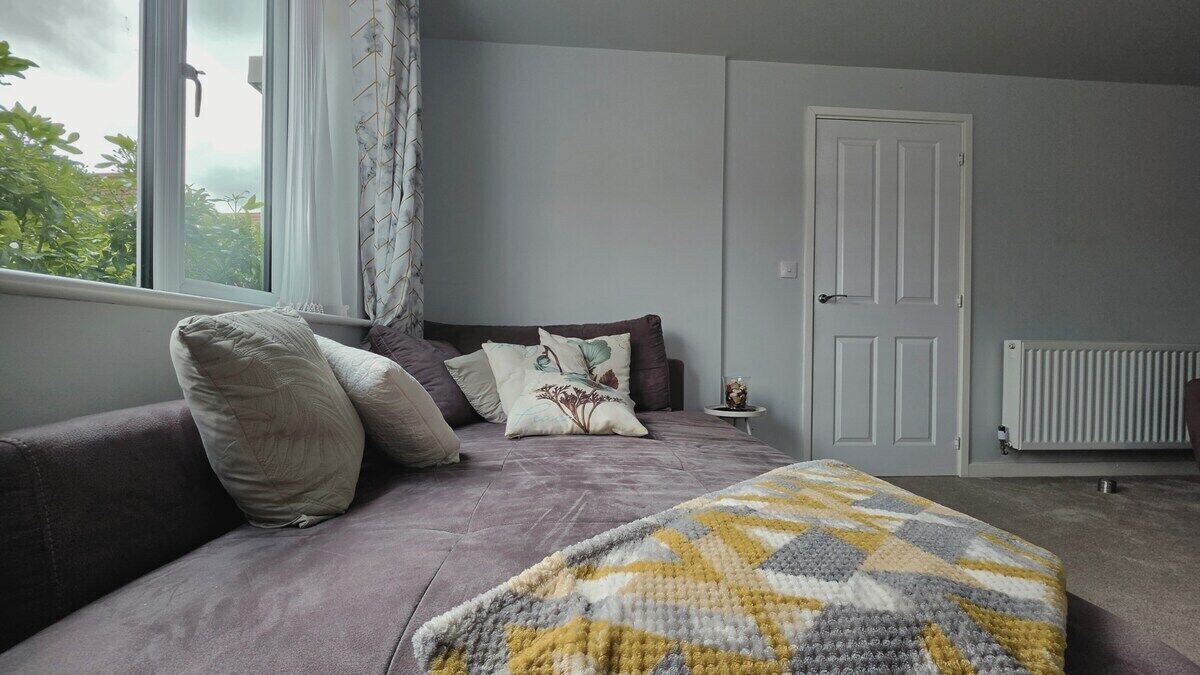 A bedroom with a bed, a window with curtains, a radiator, and a door.