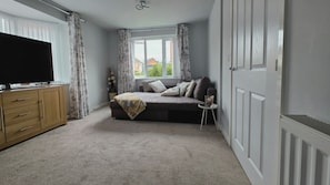 A bedroom with a bed, a TV on a wooden cabinet, a window with curtains, and a radiator.