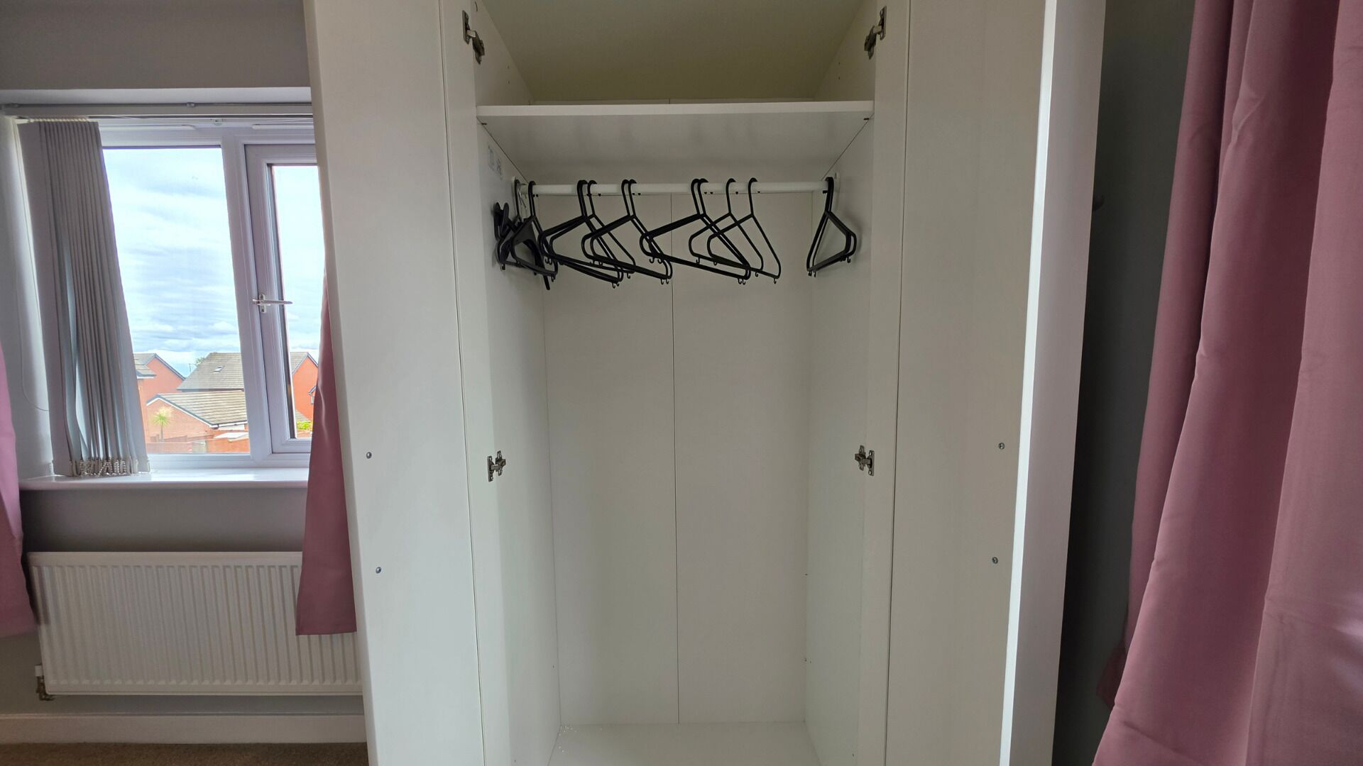 A white wardrobe with a hanging rod for clothes.